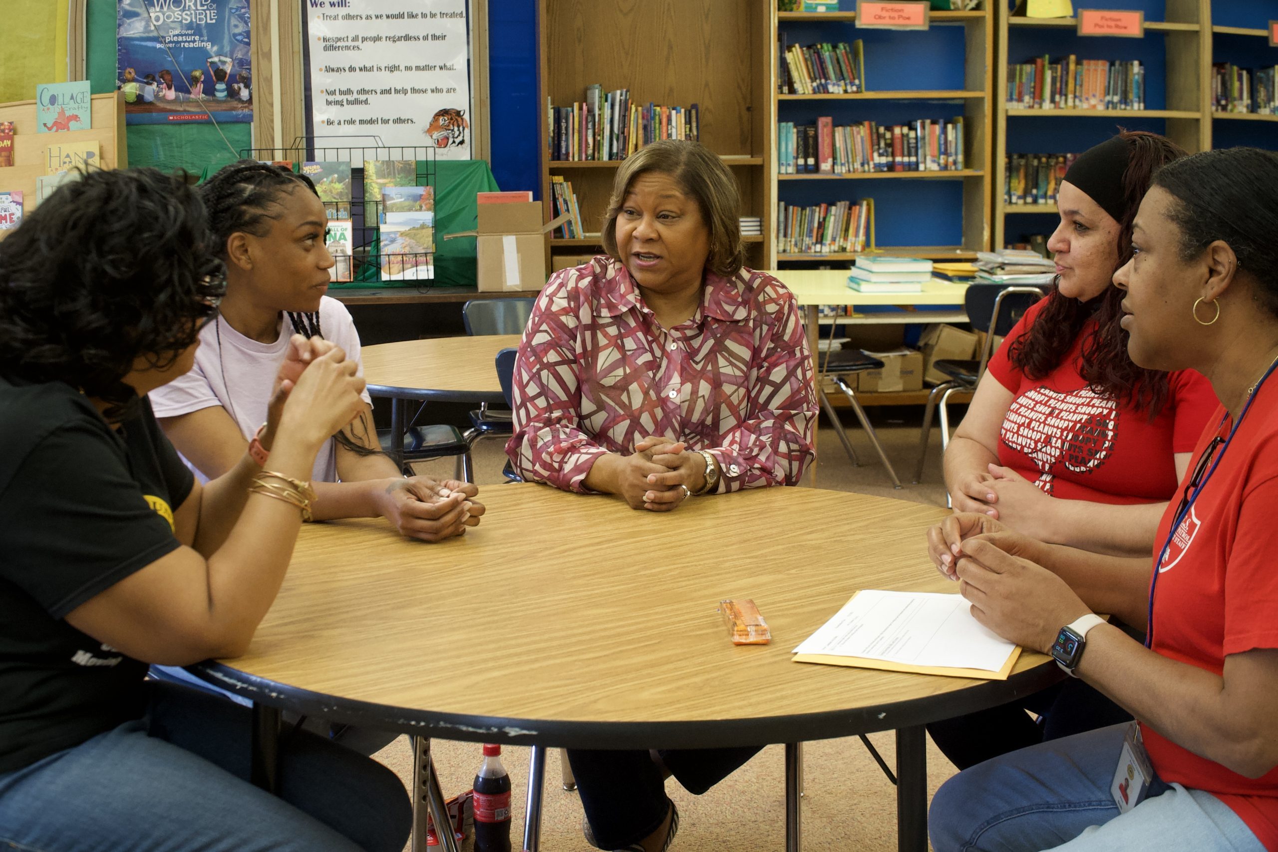 Mary Person sits at a table in a school library, engaged in discussion with four young adults.