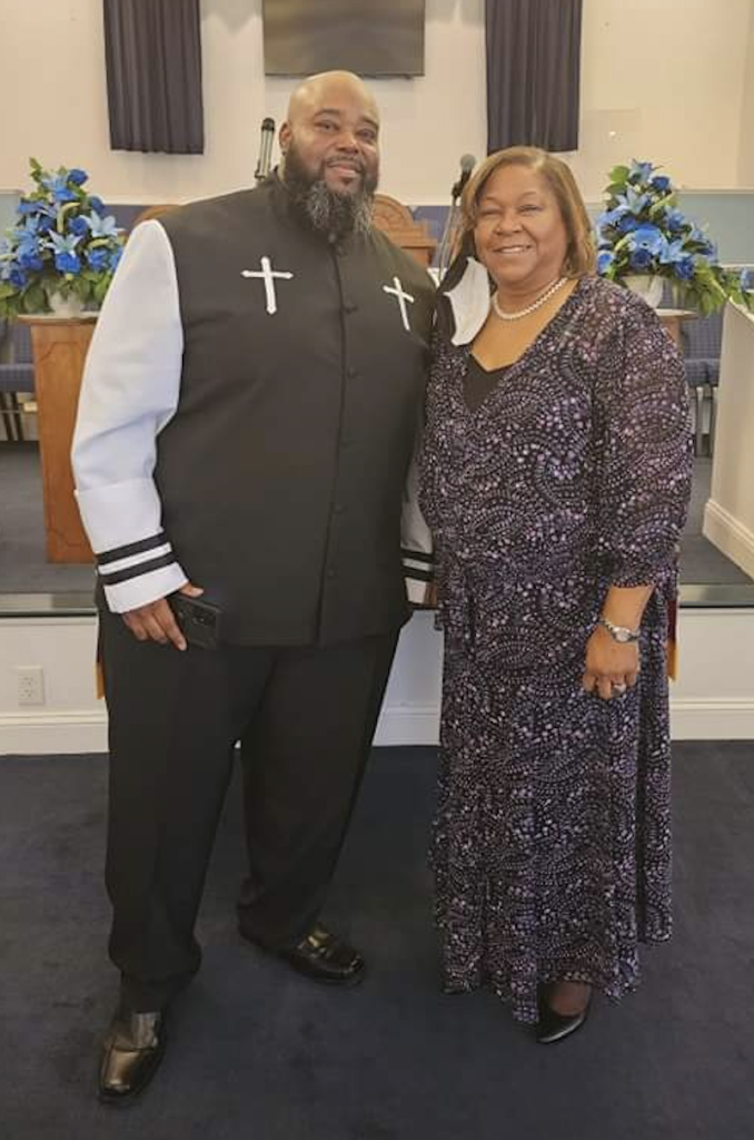 Mary Person posing and smiling with a pastor in a church sanctuary